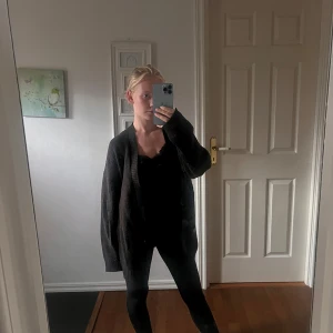 Oversized svart stickad kofta - Mysig oversized svart stickad kofta med långa ärmar och djup v-ringning. Koftan har en enkel, stilren design och är perfekt att slänga på sig över vilket outfit som helst. Passar dig som gillar en chill och avslappnad look.