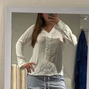 Vit blus - Säljer en vit blus med v-ringning och långa armar som man kan ha öppna eller stängda. Sidenliknande material i mitten av blusen. 