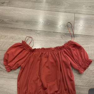 Röd offshoulder topp med puffärm - Trendig röd offshoulder topp med puffiga korta ärmar och smala axelband. Resår vid axlar och nederkant ger en snygg passform. Perfekt för dig som vill ha en luftig och stilren look.