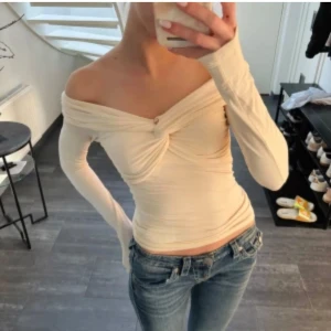 Offshoulder cremefärgad topp twistad - Säljer en superfin cremevit offshoulder topp med lång ärm och snygg twistad detalj framtill. Toppen är figurnära och har en stilren, modern look som passar perfekt till jeans eller kjol. Materialet är mjukt och stretchigt för en bekväm passform.