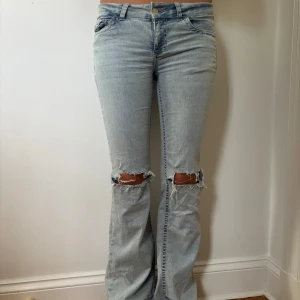 Nelly Ljusblå bootcut jeans med slitningar - Säljer ett par ljusblå bootcut jeans med slitna knän och broderade detaljer på bakfickorna. 