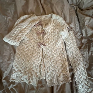 Beige stickad kofta Odd Molly med rosetter - Superfin beige stickad kofta från Odd Molly med grovt flätmönster, långa ärmar och söta rosetter framtill. Broderad logga på ena ärmen och fina detaljer!