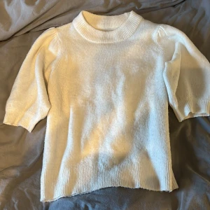 Vit stickad tröja från ONLY - Mysig vit stickad tröja från ONLY med ribbad hög hals och ribbade muddar. Tröjan har trekvartsärmar med lätt puff vid axlarna och en relaxed passform. Perfekt för lager-på-lager under höst och vinter.