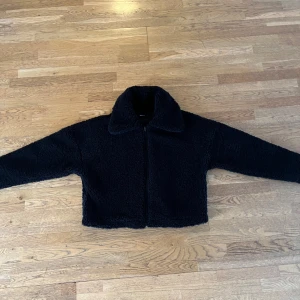 Svart teddyjacka från Gina Tricot - Mysig svart teddyjacka från Gina Tricot med dragkedja framtill och krage. Jackan har en fluffig, mjuk känsla som gör den perfekt för kyliga dagar. Enkel att styla eftersom den passar till det mesta💕💕