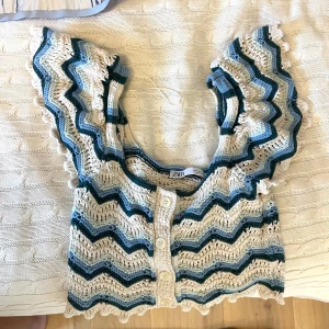 Stickad topp från Zara - Supersöt stickad topp från Zara med korta ärmar och knappar framtill. Mönstret är zigzag i beige, blått och grönt. Toppen har volangkant! Superfin 💙 passar xs-m 