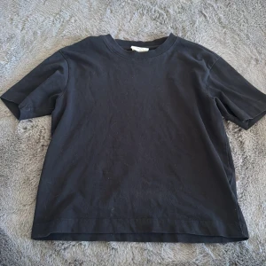 Svart basic t-shirt i bomull - Enkel svart t-shirt i klassisk modell med rund hals och korta ärmar. Tillverkad i mjuk bomull, perfekt för en clean och stilren look. Passar till allt och är ett måste i garderoben.