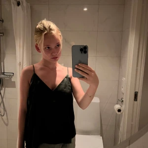 Mörkgrön satinlinne med tunna axelband - Säljer en mörkgrön linnetopp med tunna axelband och v-ringad hals. Toppen har en lös passform och är tillverkad i ett glansigt material som ger en lyxig känsla. Perfekt att styla med jeans eller kjol för en trendig look.