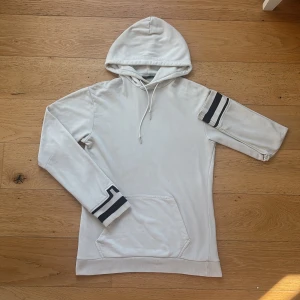 J.Lindeberg Hoodie  - Vit hoodie från J Lindeberg Ärmslutet har svarta ränder som cool detalj.  små små hål en på ärmen och en vid fickan märks knappt och kan sys enkelt. Även lite små fläckar som knappt syns men finns där ej provat behandla dom så tror de går bort !! 