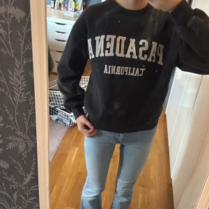 Svart sweatshirt Pasadena Gina Tricot - Cool svart sweatshirt från Gina Tricot med vit text 'PASADENA CALIFORNIA' framtill. Tröjan har rund hals, ribbade muddar och en relaxed fit. Perfekt till jeans för en chill look. Mjuk insida och klassisk collegekänsla.