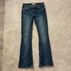 Blå bootcut jeans från Junkyard S - Snygga blå jeans från Junkyard i bootcut-modell med låg midja. Klassisk femficksdesign, slitna detaljer vid benslut och kontrastsömmar. Jeansen är gjorda i bomull och har en cool, lite vintage tvätt. Perfekta för dig som gillar retro vibe och bekväm passform.
