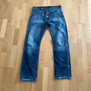 Levi's 506 blå jeans W34 L34 - Klassiska blå Levi's 506 jeans med raka ben och normal passform. Snyggt slitna detaljer och femficksmodell. Jeansen har mellanblå tvätt och är tillverkade i robust denim med tydliga kontrastsömmar. Perfekta för en avslappnad och tidlös look.
