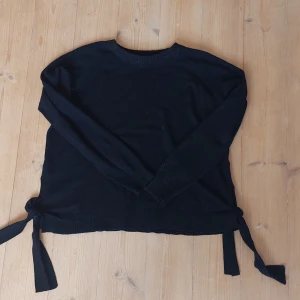  stickad tröja  - Svart stickad tröja med rund hals och långa ärmar. Tröjan har snygga knytband i båda sidorna nertill som ger en extra detalj. Perfekt för lager-på-lager och funkar året runt. Enkel och stilren design som passar till det mesta.
