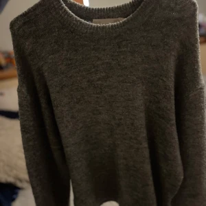 Mörkgrå stickad tröja - En enkel och stilren mörkgrå stickad tröja med rund halsringning och långa ärmar. Perfekt för lager-på-lager och passar till både jeans och kjol. Mjuk och skön känsla, perfekt för kyligare dagar.