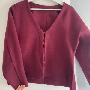 Vinröd kofta med v-ringning och knappar - Vinröd kofta med v-ringad hals och snygga knappar framtill. Långärmad och i stickat material, perfekt för lager-på-lager. Snygg slits i sidorna för extra detalj. Enkel att matcha och supermjuk mot huden.