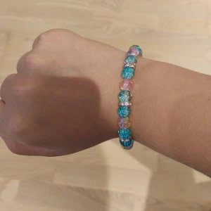 Färgglatt pärlarmband med glitter - Säljer ett armband med runda pärlor i blått, rosa, gult och silver. Pärlorna har en glittrig yta och är trädda på elastisk tråd. Perfekt för dig som gillar färg och vill ha något som sticker ut lite extra.