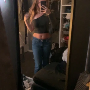 Svart oneshoulder croppad topp - Säljer en svart croppad topp med oneshoulder-design och lång ärm på ena sidan. Sitter tight och har en stilren look som passar perfekt till jeans eller kjol. Enkel och snygg att styla för en trendig outfit.