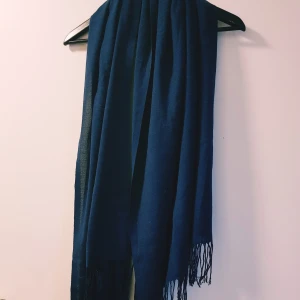 Mörkblå halsduk med fransar - En stilren mörkblå halsduk med tunna fransar i ändarna. Halsduken är mjuk och lätt, perfekt att slänga över axlarna för extra värme. Enkel design utan mönster, passar till de flesta outfits.  Helt skick dock noppror
