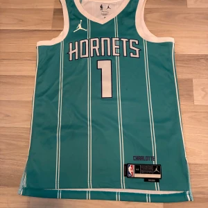 Charlotte Hornets Ball basketlinne M - Snyggt Charlotte Hornets basketlinne med Ball #1, i turkos med vita ränder och vita detaljer. Jordan-logga på bröstet och Dri-FIT-material som andas. Perfekt för basket eller streetwear. Klassisk NBA-stil med v-ringning och ärmlös design.