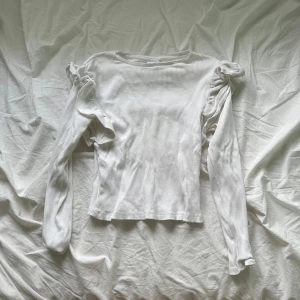 Vit ribbad långärmad tröja Zara - Supersöt vit ribbad tröja från Zara med långa ärmar och volangdetaljer på axlarna. Tröjan har en tight passform och är tillverkad i mjuk bomull, perfekt för dig som gillar stilrena och feminina plagg.