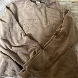 Beige fleece-tröja med strassdetaljer - Mjuk och mysig beige fleece-tröja med lång ärm och rund hals. Framsidan har texten 'Faith' i glittrande strass, vilket ger en snygg och trendig look. Perfekt för kyliga dagar när du vill vara både bekväm och stilren. Har en liten grön fläk på armen men man märker inte av det om man inte kollar noga🥰