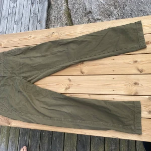 Olivgröna chinos i bomull - Snygga olivgröna chinos med raka ben och klassiska fickor både fram och bak. Byxorna har bälteshällor och är tillverkade i mjuk bomull. Knappt använda. Osäker på storleken men skulle säga de är M/S