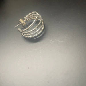 Silvriga creolörhängen med flera bågar - Snygga silvriga creolörhängen med flera parallella bågar i ett flätat mönster. De har en cool och modern design som sticker ut och passar perfekt om du vill ha något unikt. Stift och lås i samma färg. Perfekt accessoar för att lyfta din stil.