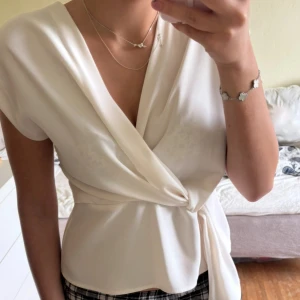 Vit omlottopp från Zara - Säljer en stilren vit omlottopp från Zara i storlek S. Toppen har korta ärmar, v-ringning och knyt i midjan som ger en snygg siluett. Perfekt att matcha med både jeans och kjol för en fräsch look.