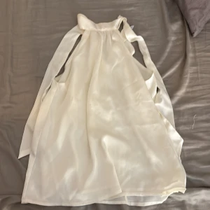 Vit top i satin - Superfin vit top i glansigt satinliknande material. Toppen har breda knytband vid axlarna och en luftig, flowy passform. Perfekt för sommarens alla tillfällen när du vill känna dig extra chic.