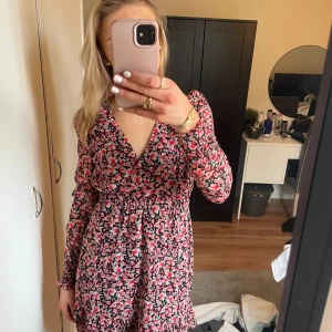 Blommig klänning med v-ringning - Säljer en söt blommig klänning med v-ringning och långa ärmar. Klänningen har ett fint mönster i rosa, rött och vitt. Perfekt för vår och sommar! 🌸