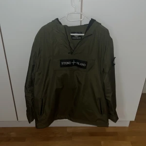Grön vindjacka från Stone Island - Säljer en stilren grön vindjacka från Stone Island. Jackan har en dragkedja framtill och en praktisk ficka med lock på bröstet. Den har långa ärmar och en justerbar huva. Perfekt för blåsiga dagar.