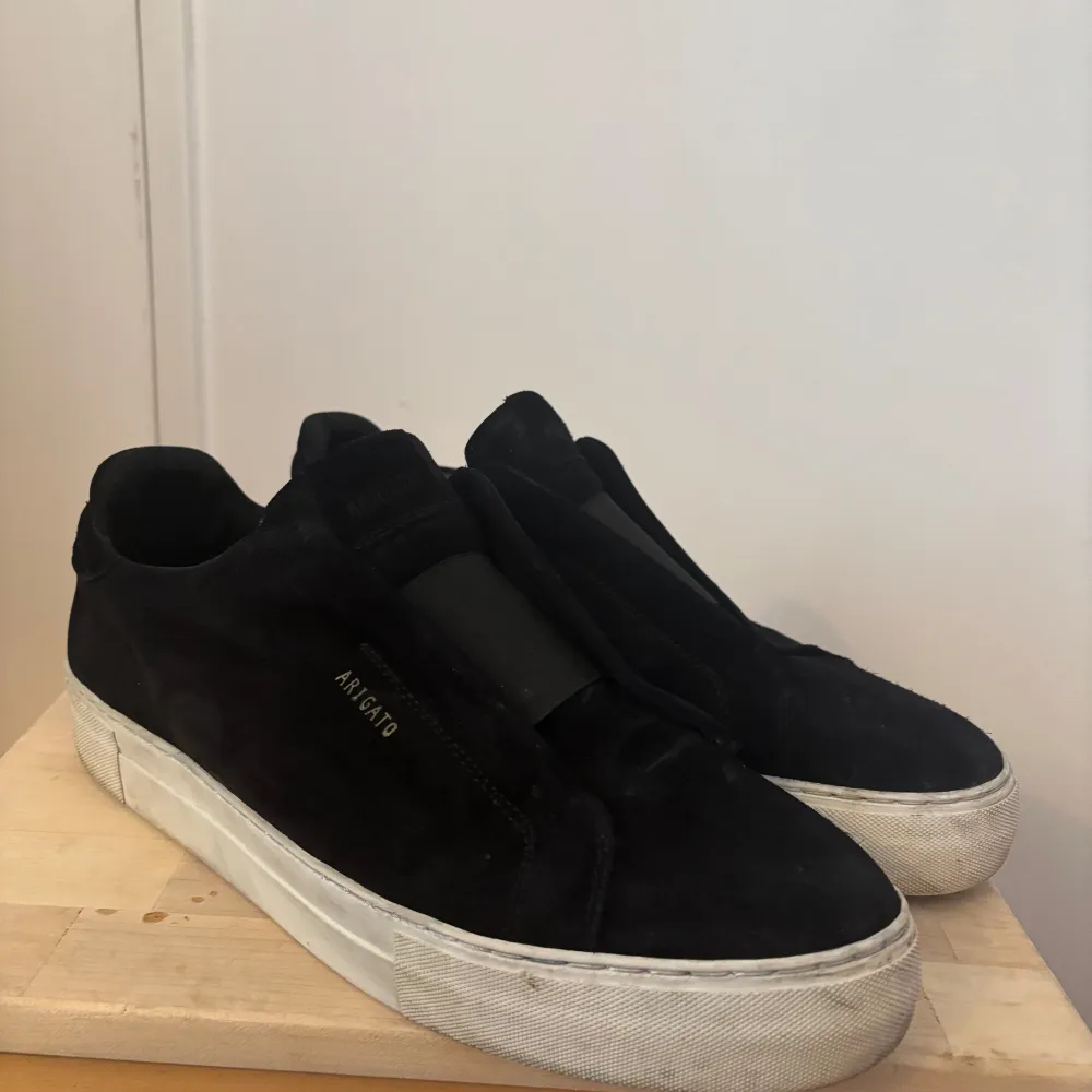 Snygga svarta sneakers från Axel Arigato med en stilren design. Skorna har en vit sula som ger en fin kontrast till det svarta. Perfekta för en casual look. . Kengät.
