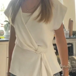 Vit omlottopp från Zara - Säljer en stilren vit omlottopp från Zara. Toppen har korta ärmar och en knytning i sidan som ger en elegant look. Perfekt för både vardag och festliga tillfällen.