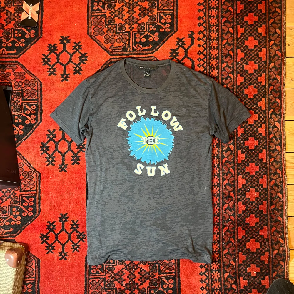 Säljer en grå t-shirt från Marc by Marc Jacobs med texten 'Follow the Sun' i vitt och en blå sol i mitten. Perfekt för en avslappnad stil.. T-paidat.