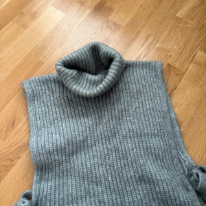 Grå ribbad polotröja - Snygg grå ribbad polotröja med hög krage och knytband på sidorna. Perfekt för kyliga dagar när du vill hålla dig varm och stilren. Superbra skick. Storlek L/M. Varm och mysig 