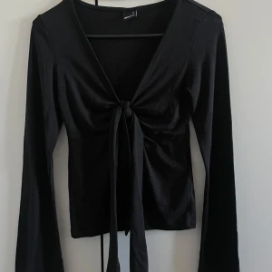 Svart långärmad topp med knyt - Snygg svart långärmad topp från Bershka med knyt framtill. Perfekt för en stilren look, passar både till jeans och kjol. Toppen har en v-ringad design som ger en elegant touch.