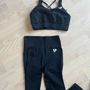 Womens best träningstaights och topp - Snygg svart sporttopp med korsade band i ryggen och ribbad kant. Perfekt för träning och ger bra stöd. Tajts som hör till. Ribbade med hög midja. mkt sköna