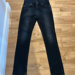 Svarta jeans från Nudie Jeans - Snygga svarta jeans från Nudie Jeans med klassisk femficksdesign. De har en diskret broderad detalj på bakfickan och en mörk tvätt som ger en stilren look. Perfekta för en avslappnad stil.