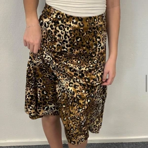 Leopardmönstrad kjol - Snygg leopardmönstrad kjol i bruna och svarta toner. Kjolen har en omlott-design som ger en fin drapering och rörelse. Perfekt för att ge en djärv touch till din outfit.💕🐆