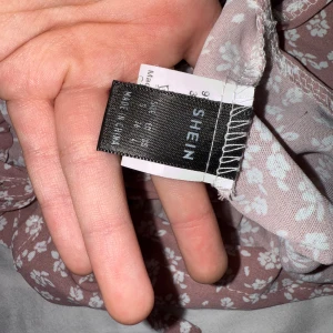 Blommig topp från Shein - Säljer en söt blommig topp från Shein i en mjuk rosa nyans med vita blommor. Toppen har en elastisk midja och smala axelband, perfekt för varma dagar.