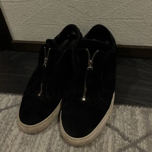 Arigatos skor - Snygga svarta sneakers med dragkedja framtill. Skorna har en stilren design med en vit sula som ger en cool kontrast. Perfekta för en avslappnad stil.