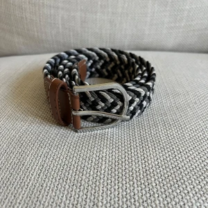 Svart och vitt flätat bälte - Snyggt flätat bälte i svart och vitt med bruna läderdetaljer och ett silverfärgat spänne. Perfekt för att ge en stilren touch till din outfit.