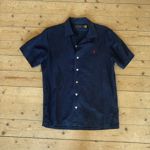 Mörkblå linneskjorta skjorta från Polo Ralph Lauren - Säljer en stilren mörkblå kortärmad linne skjorta från Polo Ralph Lauren. Den är bara använd ett fåtal gånger och är i väldigt bra skick. Skjortan är strl S