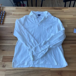 Vit långärmad pikétröja från Riley - Säljer en stilren vit långärmad pikétröja från Riley i 100% bomull. Tröjan har en klassisk krage och en bröstficka. Perfekt för en avslappnad men ändå snygg look. Passar bra till både jeans och chinos. Passar XS bra skick