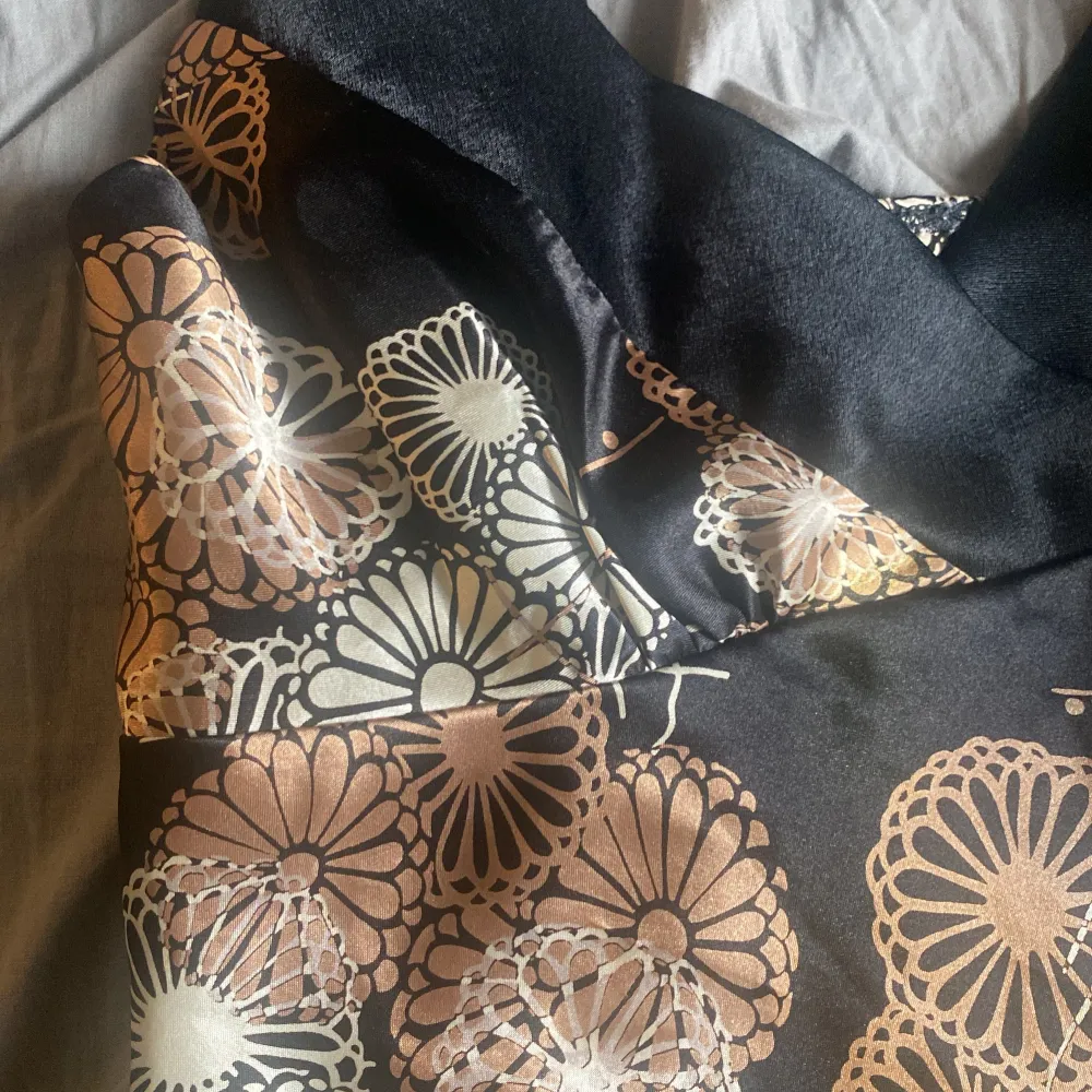 Snygg svart blus med blommigt mönster i beige och vitt. Blusen har tunna axelband och en elegant passform. Perfekt för en somrig dag eller en kväll ute. 🌸. Puserot.