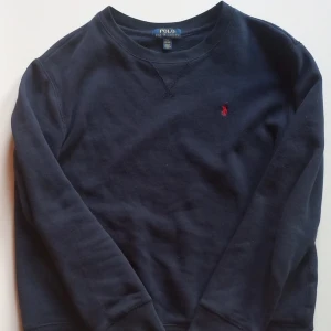 Mörkblå tröja från Polo Ralph Lauren - Säljer en snygg mörkblå Polo Ralph Lauren-tröja i storlek L (14-16 år). Väldigt skön och stilren! Tyvärr lite för liten för mig nu, därför säljer jag den. Skick: 6/10, finns ett litet hål i högerarmen (se bild). Perfekt som vardagströja! Skickar fler bilder vid intresse!