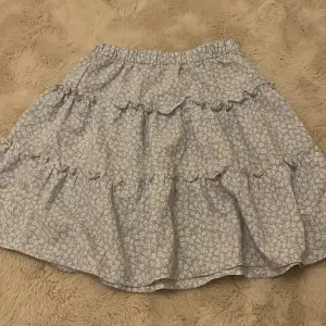 Söt blommig kjol från H&M i ljusblått med vita blommor. Kjolen har volanger och en elastisk midja för en bekväm passform. Perfekt för en somrig look!
