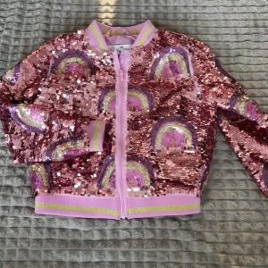 Rosa paljettjacka med regnbågsmönster - Säljer en glittrig rosa jacka med paljetter och regnbågsmönster. Jackan har dragkedja framtill och långa ärmar. Perfekt för att lysa upp vilken outfit som helst! 🌈✨