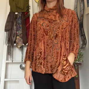 Orange stickad tröja med mönster - Köpt secondhand och har använts en del. Unik stickad orange tröja med sammet med intrikat mönster och trekvartsärmar. Tröjan har en lös passform och dekorativa detaljer framtill. Perfekt för att ge en bohemisk touch till din garderob.