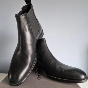 Svarta Chelsea boots från Vagabond - Snygga svarta Chelsea boots från Vagabond i skinn. De har en klassisk design med elastiska paneler på sidorna och en dragflik baktill för enkel påtagning. Perfekta för en stilren look. Nypris 1400kr använda max 3 gånger.
