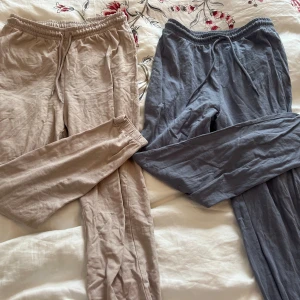 Beige och blå mjukisbyxor - Två par mjukisbyxor i mjukt material, ett par i beige och ett i blå. Båda har elastisk midja med snörning för justerbar passform. Perfekta för en avslappnad stil. 100 kr för båda
